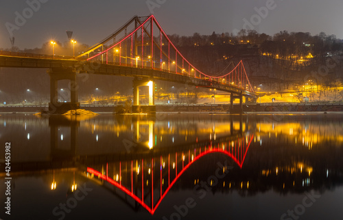 Pedestrian bridge in Kiev. Evening lighting. Reflection of the bridge in the river.