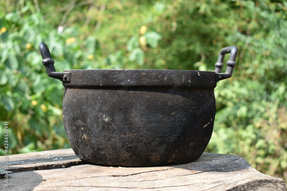 The old black pot was empty on the table. It has a green blurred background. The old black pot was empty on the table. It has a green blurred background.