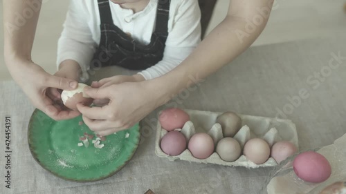 Kid's hands are cleaning colorful Easter eggs. Mom and son are cleaning Easter eggs. Little boy eating Easter egg