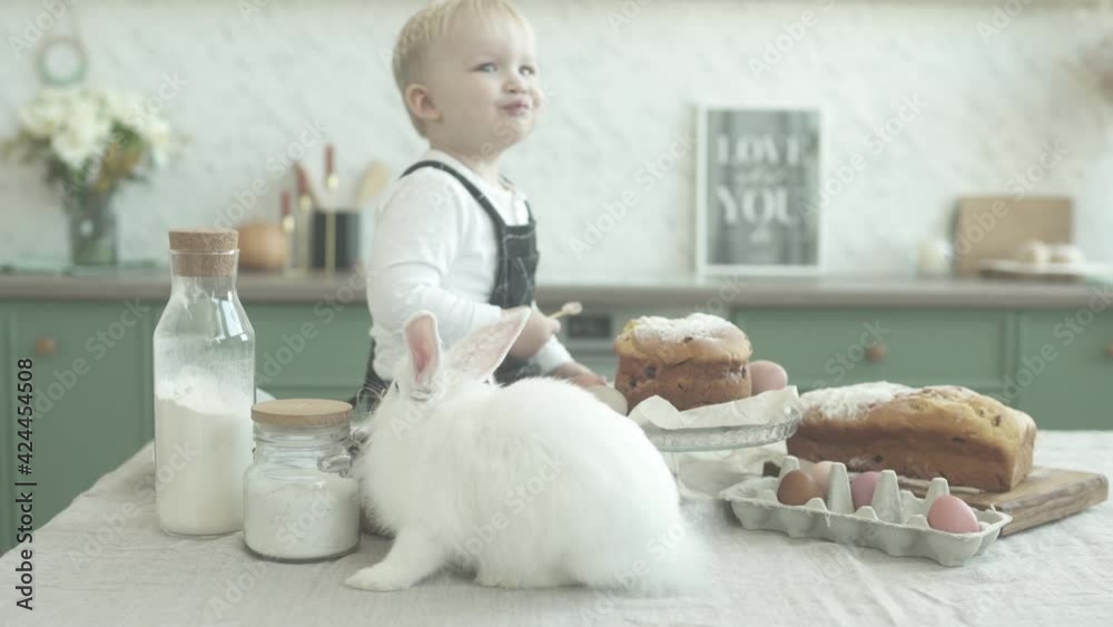 Little boy eats Easter bread while sitting at the festive table. Next to a mother with a little girl in her arms Little boy eats Easter bread while sitting at the festive table. Next to a mother with a little girl in her arms