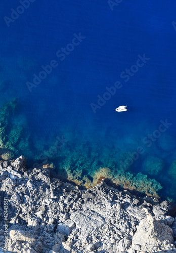 Top view to the blue transparent ocean a rocky cliff and a white boat  diving and snorkeling spot from above 
