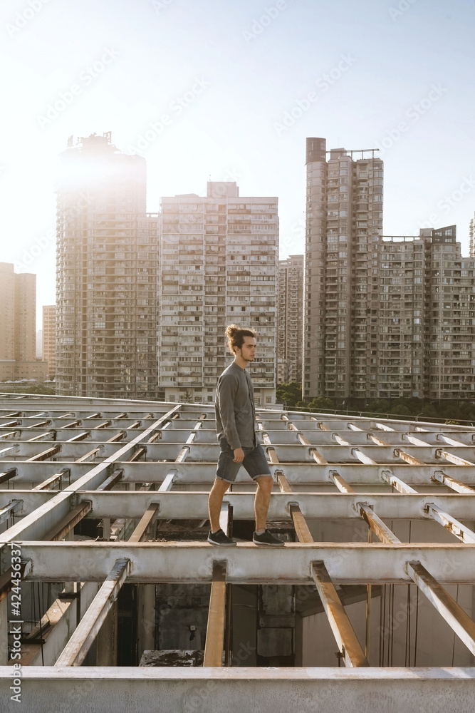 Man walking on the rooftop, wearing casual, curly hair collected in the pony tail. Background of residential building. Urban rooftopper extreme lifestyle, cityscape, abandoned atmosphere Man walking on the rooftop, wearing casual, curly hair collected in the pony tail. Background of residential building. Urban rooftopper extreme lifestyle, cityscape, abandoned atmosphere