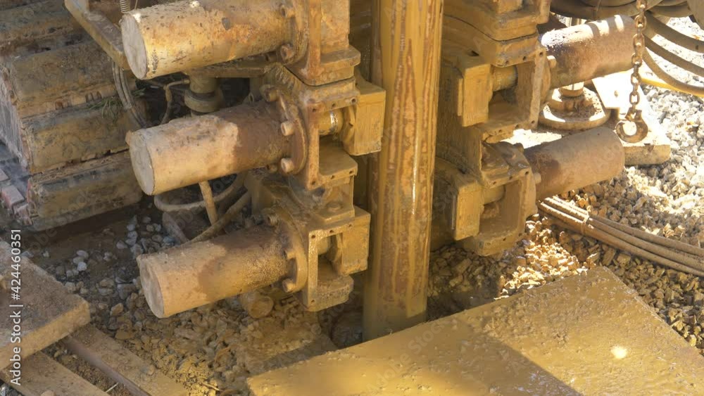 CLOSE UP: Massive drill spins and drills into the soil at a construction site in the sunny countryside. Heavy industrial rig bores a hole in the ground during modern geothermal pump installation. CLOSE UP: Massive drill spins and drills into the soil at a construction site in the sunny countryside. Heavy industrial rig bores a hole in the ground during modern geothermal pump installation.