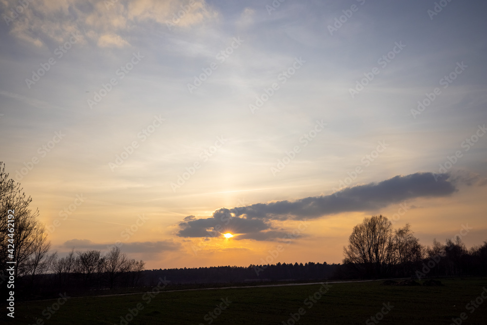 Sunset cloudy sky with picturesque clouds lit by warm sunset sunlight, colorful sunset sky with dramatic sky clouds lit by evening sunlight. Country road at sunset. High quality photo