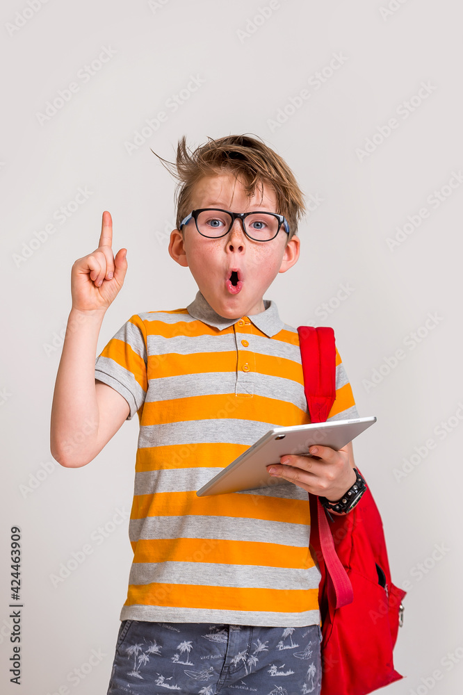 education, technology and internet. Boy reading an e-book instead of books. Caucasian 7 years old boy with tablet computer pointing up with a finger. Portrait of happy school boy with backpack education, technology and internet. Boy reading an e-book instead of books. Caucasian 7 years old boy with tablet computer pointing up with a finger. Portrait of happy school boy with backpack