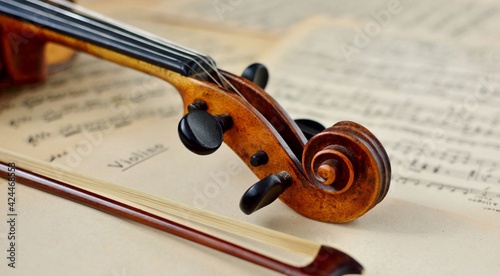 An old antique violin and a bow on a table with yellowed sheet music close-up.
