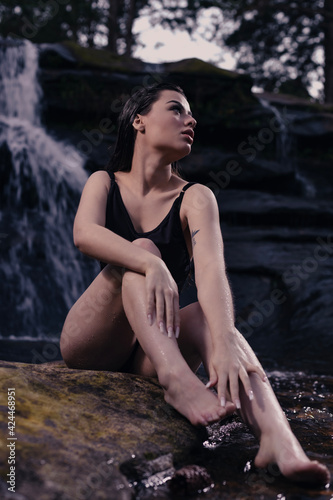 young woamn model posing for fashion photoshoot in a waterfall with long black hair and black swimsuit