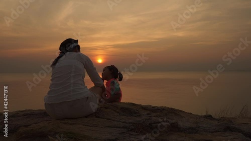 Asian mother and daughter sitting at cliffe against sunset scape at ocean. photo