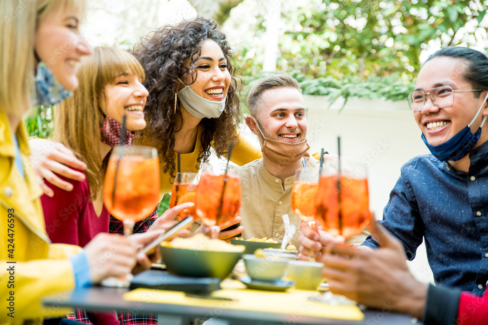 Multiracial friends wearing face masks drinking cocktails at bar restaurant - New normal friendship concept with young people enjoying meal in backyard party - Focus on guy in the middle Multiracial friends wearing face masks drinking cocktails at bar restaurant - New normal friendship concept with young people enjoying meal in backyard party - Focus on guy in the middle