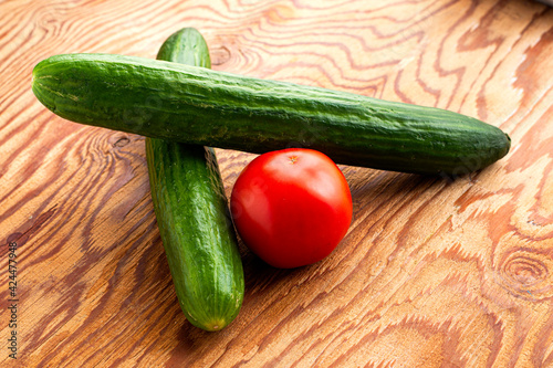 two cucumbers and a tomato on a wooden surface