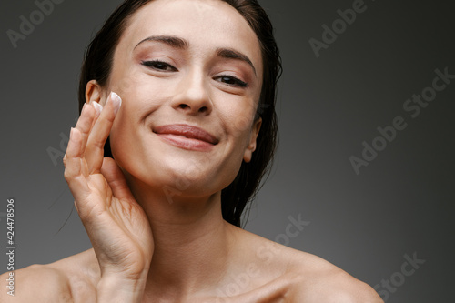 Smiling mod aged brunette woman applying facial cream photo