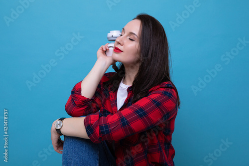 A young woman in a red shirt listens to music on a blue background