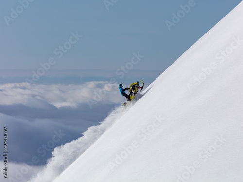 snowmobiler rides to the top of a steep wall-above the clouds. flying to the peak of the mountain on a turbocharged snowmobile. copy space. high resolution photo