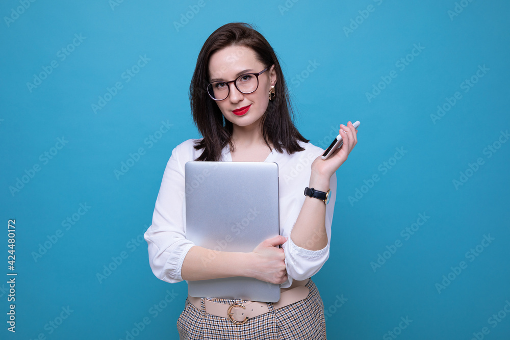 Portrait of a young brunette woman with a laptop and phone on a blue background Portrait of a young brunette woman with a laptop and phone on a blue background