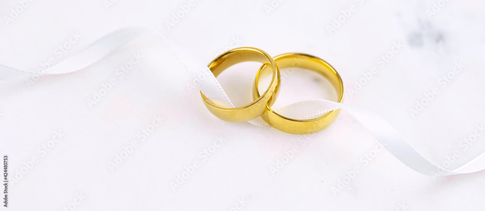 Banner with two golden wedding rings close up with ribbon on white ...