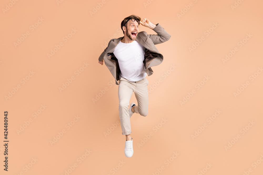Full length photo of amazed shocked young man look empty space jump run isolated on pastel beige color background Full length photo of amazed shocked young man look empty space jump run isolated on pastel beige color background