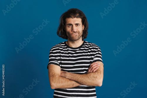 Displeased brunette man in striped t-shirt posing with arms crossed