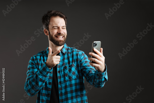 Bearded laughing man pointing finger at camera while taking selfie on cellphone © Drobot Dean