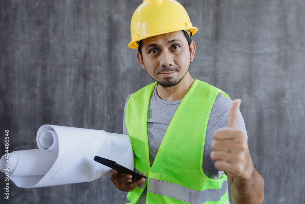 Fototapeta premium Asian construction worker hold blueprint and smartphone with making thumb up sign like