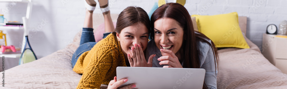 positive mother and teenage girl watching movie on laptop in bedroom, banner positive mother and teenage girl watching movie on laptop in bedroom, banner