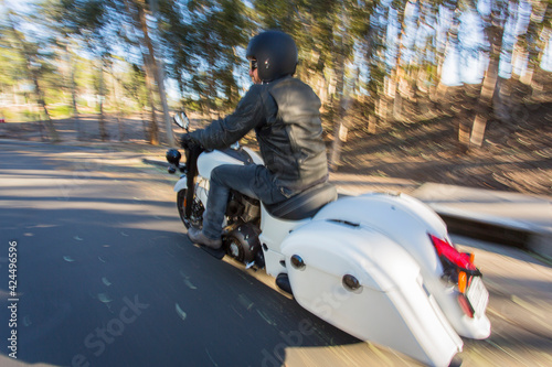 Motorcyclist dressed in leathers riding down a canyon street with trees blurred photo