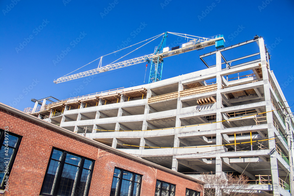 Parking garage under construction - slanted view of concrete bones of building with giant crane on top with lower pre-existing brick building in foreground