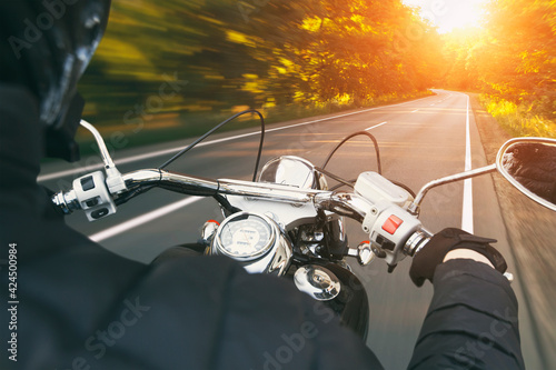 The motorcyclist is riding through the empty asphalt road in the evening