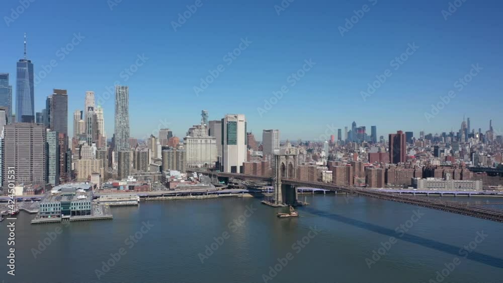 An aerial view over the East River on a sunny day with blue skies. The camera, facing the Brooklyn and Manhattan bridges, pan left over the unusually quiet river with Manhattan in the background. An aerial view over the East River on a sunny day with blue skies. The camera, facing the Brooklyn and Manhattan bridges, pan left over the unusually quiet river with Manhattan in the background.
