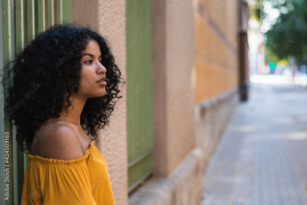 Woman with curly hair and yellow shirt looking away in the street