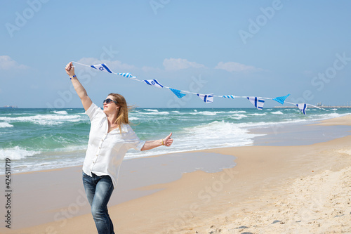 Girl with a garland of Israel flags shows a finger an excellent sign on the seashore. Patriotic holiday Independence day Israel - Yom Ha'atzmaut concept. photo