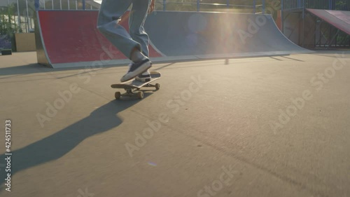 Handheld tracking shot of teenager in jeans skating and doing kickflip in skatepark