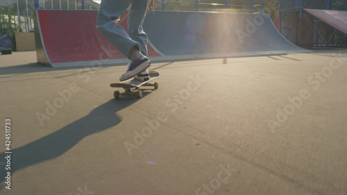 Handheld tracking shot of teenager in jeans skating and doing kickflip in skatepark photo