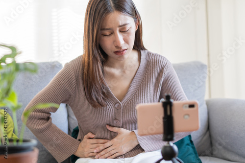 Flatulence asian young woman, girl or Patient hand in stomach ache suffer food poisoning, abdominal pain and colon problem, gastritis or diarrhoea.Telemedicine or telehealth on smartphone concept.