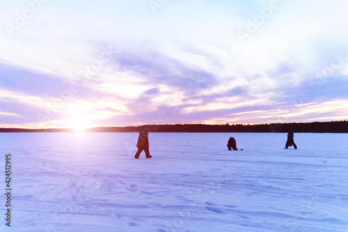 silhouettes of fishermen on a winter lake at sunset fishing. Winter landscape, winter sports