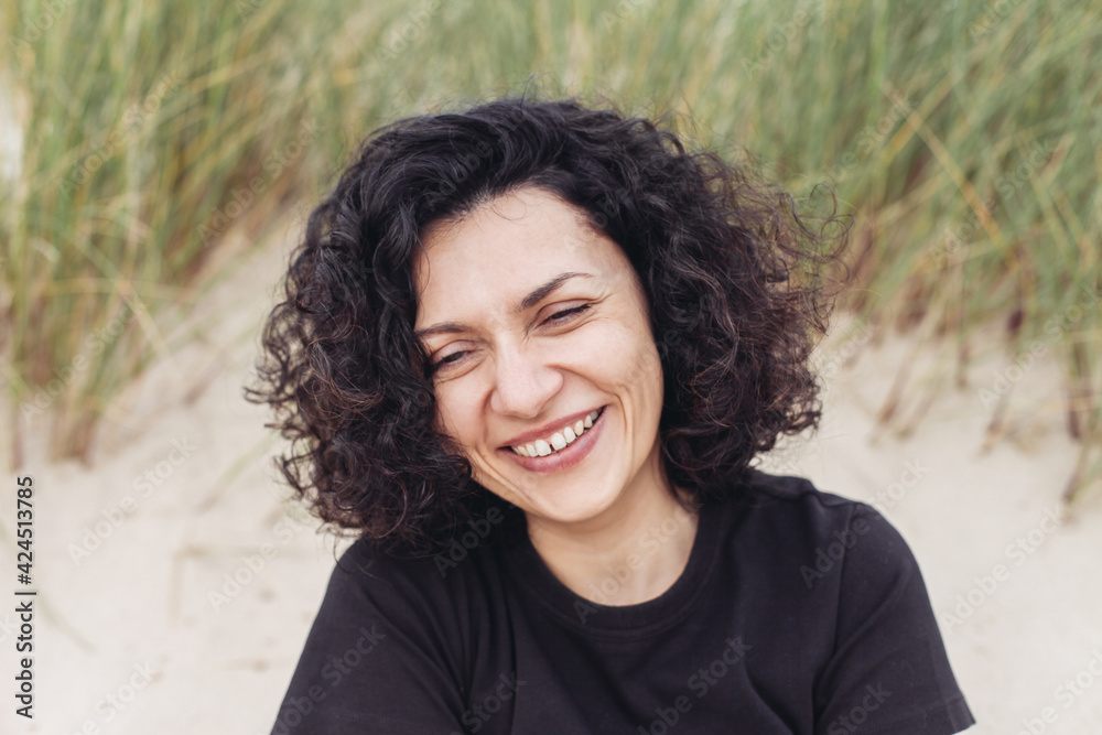 A brunette woman laughing and looking down, on a beach 