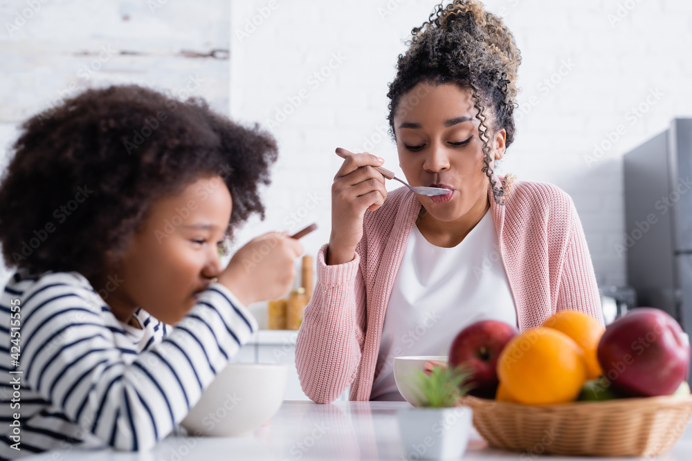african american mother and daughter having breakfast near fruits on blurred foreground