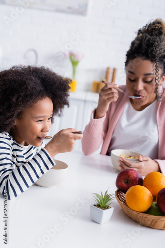 african american mother and daughter eating tasty corn flakes for breakfast