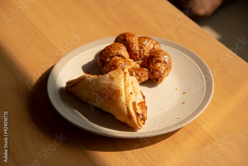 Morning croissant and pie in white plate on wooden table