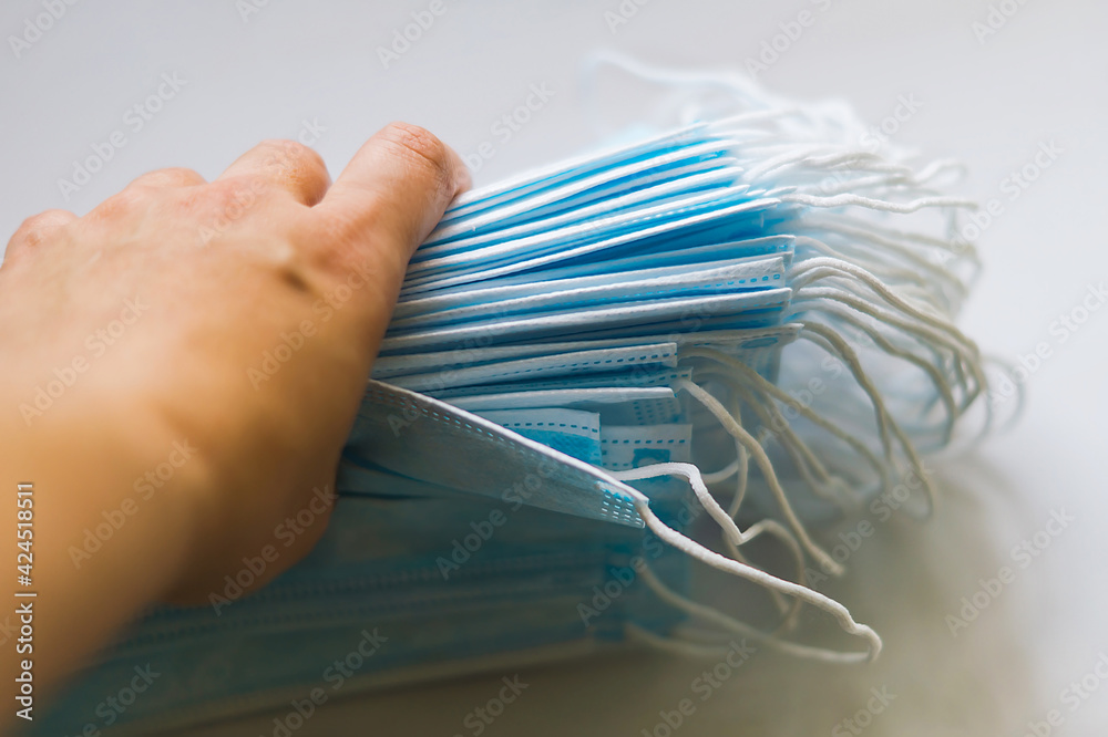 Fototapeta premium A woman's hand holds a stack of disposable medical masks for protection against viral diseases in close-up. Medical surgical blue masks in the hands of a female doctor. Prevention of diseases