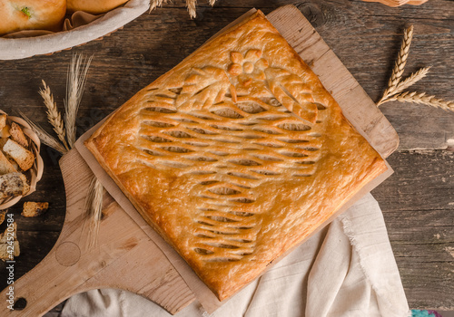 Delicious fresh square pie stuffed with curly dough decorations on wooden photo