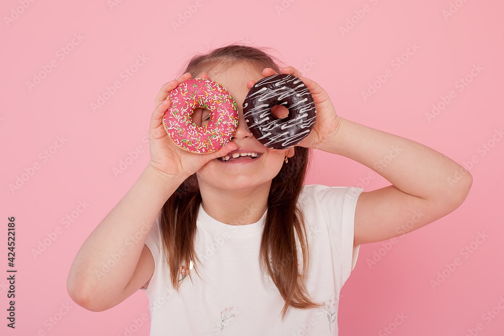 young beautiful happy and excited blond girl 8 or 9 years old holding two donuts on her eyes looking through them playing cheerful in sugar calories and unhealthy sweet nutrition abuse addiction.