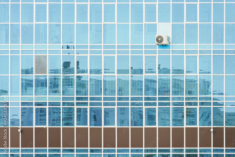 A fragment of the glazed facade of a building with a single air conditioner and a reflection in the glass of the building opposite. Copy space.