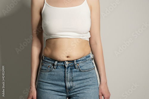 Skinny fat figured unrecognizable woman with belly fat. Woman`s hips closeup raw studio shot in grey background. Dieting and fat loss concept. © transurfer