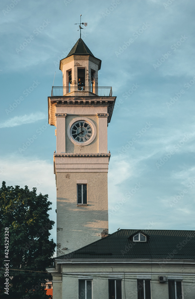 Antique brick signal tower with a clock against a blue evening summer sky. The building of the old fire station in the city of Poltava, Ukraine. Old architecture of Eastern Europe