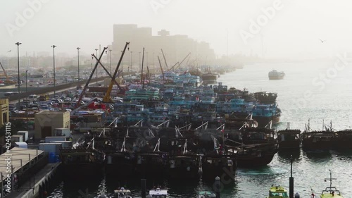 Dhow Boat Maneuvering At Crowded Port In Dubai Creek With Working Cranes in Dubai, UAE. - wide shot photo