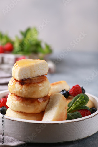 Healthy breakfast. Cheesecakes, cottage cheese pancakes with honey, fresh berries, mint on a white wooden plate on a gray table. Background image, copy space, vertical