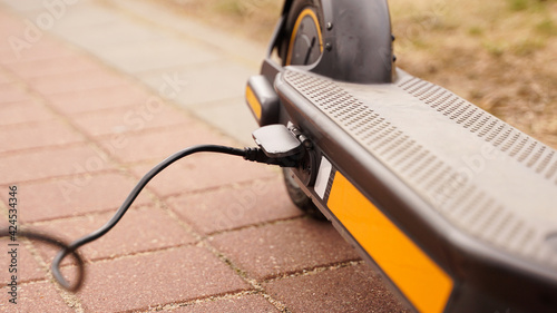 The electric scooter is charging outdoors. The wire runs into the camera.