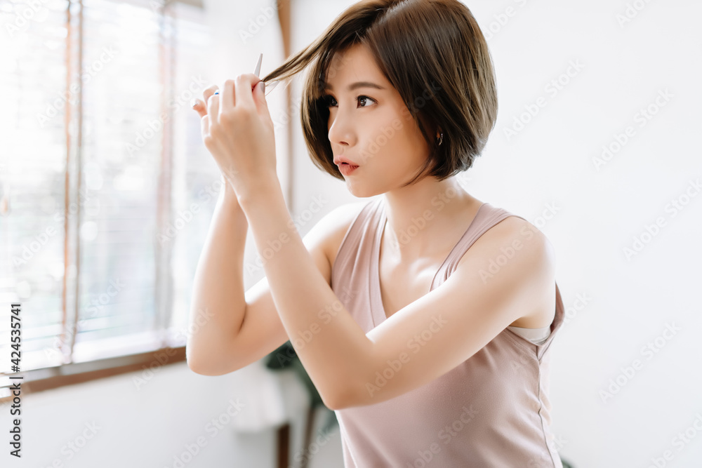Portrait of beauiful young Asian woman having her hair cut with scissors at  home. She's stay at home during the coronavirus pandemic, Self hair care  during quarantine. Stock Photo | Adobe Stock