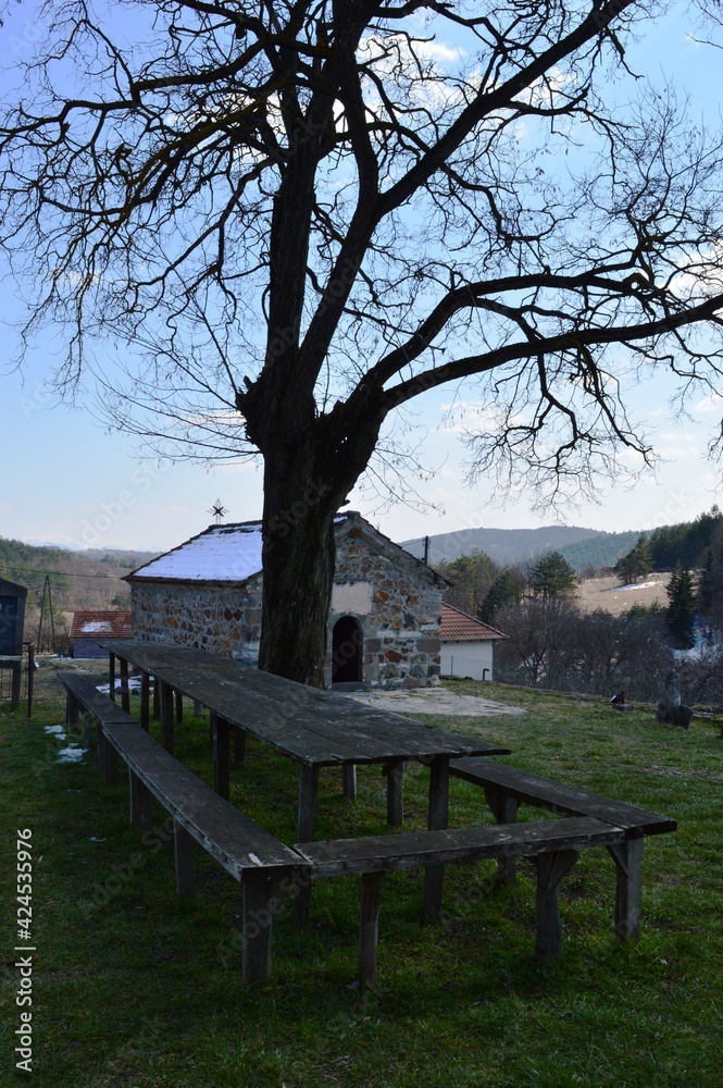 benches and a table in front of an old small, stone Orthodox church benches and a table in front of an old small, stone Orthodox church