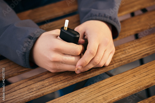 Young adult man outside and smoking tobacco device electronic cigarette heater. Smoke and steam system with sticks inside, image with copy space. Harmful habit harm to health lungs 